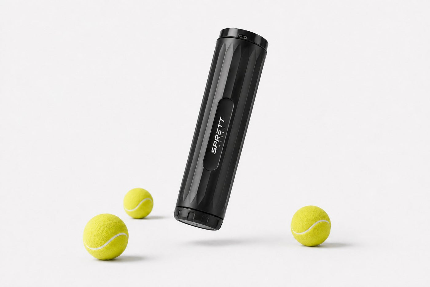 SprettBoks svevende på skrå med tre tennisballer på et lyst studiogulv